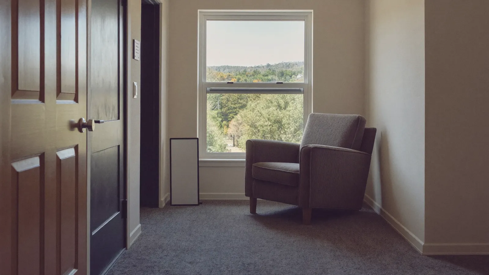 An empty armchair by a sunny window in a senior living apartment awaiting a new resident