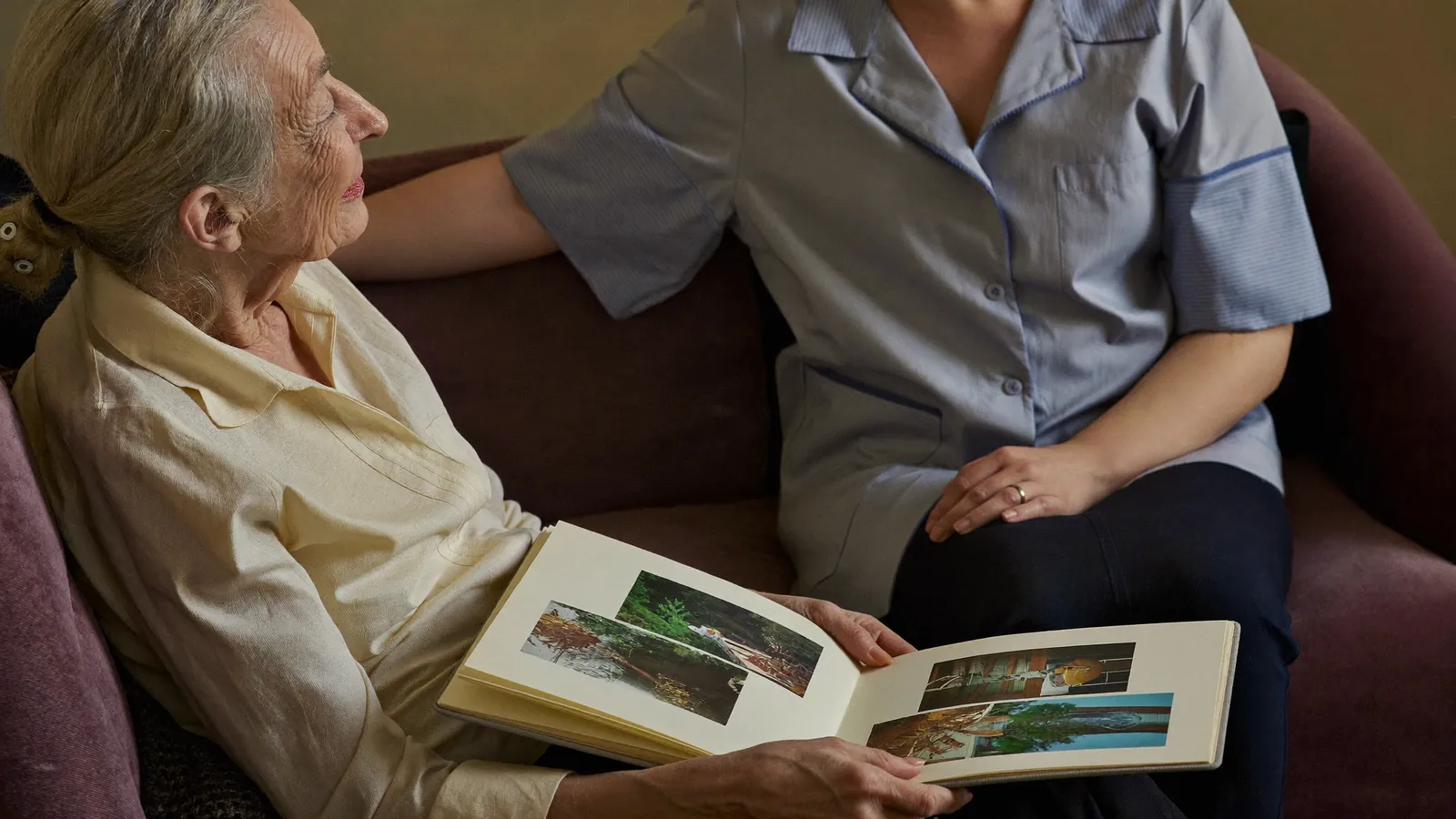 An older woman looking through a photo album with a caregiver beside her