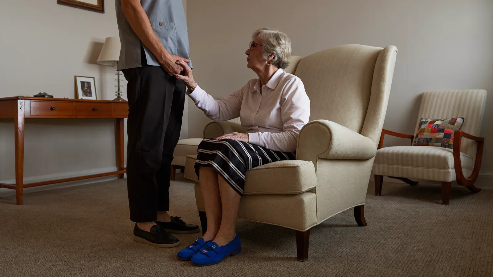 A caregiver holding the hand of an older woman in a calm memory care sitting room