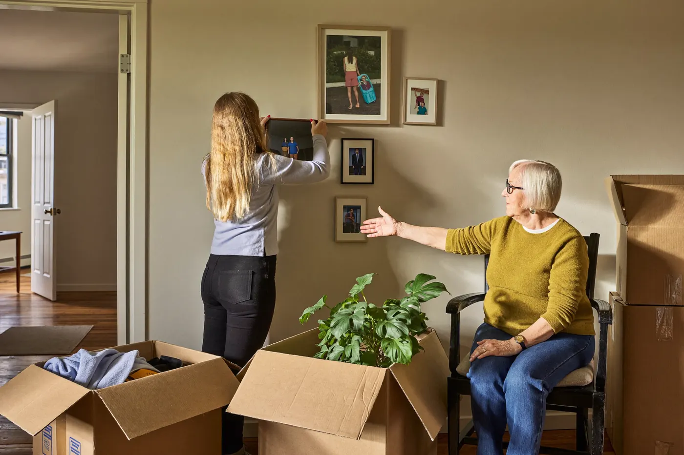 An adult daughter hangs family photos in her mother's new senior apartment on move in day